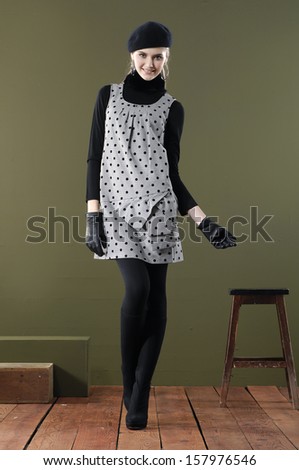 Full length portrait of young woman in hat with wooden cube posing wooden floor