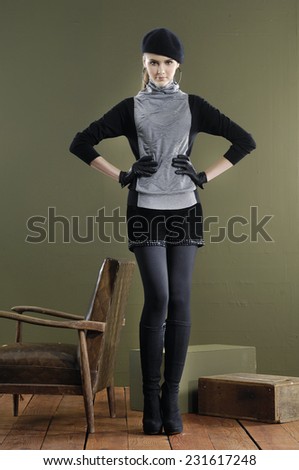 Full length Beautiful fashion girl in hat standing near chair with cube on wooden floor