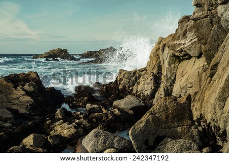 Large rocky beach with waves crashing over the rocks of Monterey California with blue skies above and crystal blue water below