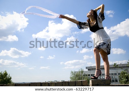 The beautiful woman in an easy years dress on a background of the blue sky and snow-white clouds
