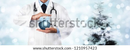 Merry Christmas from doctor,, best wishes concept, hands with xmas ball on blurred light and tree, gift card banner web template with copy space