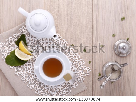 teapot with cup of tea, tea bag, lemon, sugar,