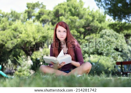 student sitting in the park with a book looking up