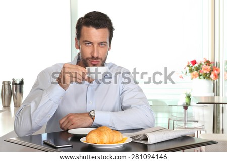 man drinking coffee in cafe with croissant and newspaper on table