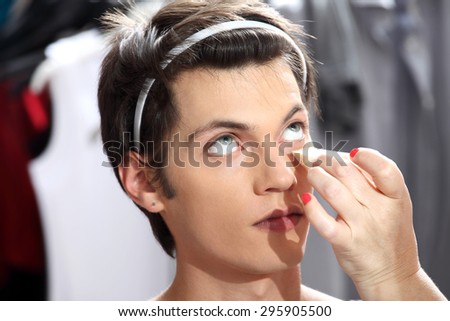 makeup artist applying foundation with a sponge, man in the dressing room mirror