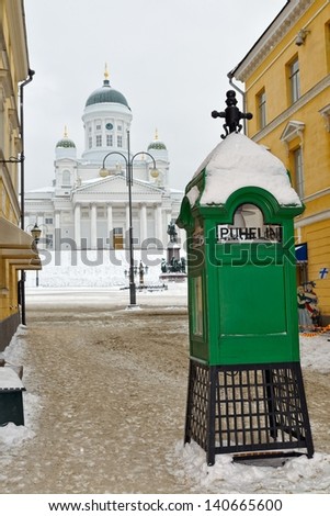Traditional old public phone box with Statue of Alexander II, emperor of Russia, in front of Helsinki Lutheran Cathedral at background in winter morning