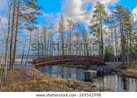 Wooden footbridge across the channel between lakes at autumn forest in Finland