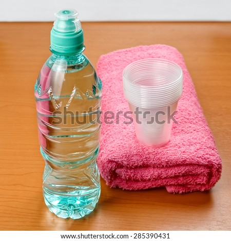 Bottle of water, towel and plastic cups on wooden table