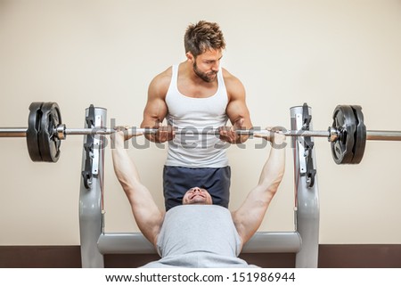 A handsome young muscular sports man doing weight lifting and gets help from his friend