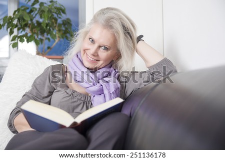 An image of a beautiful woman reading a book on her sofa