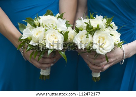 two bridesmaids in blue holding wedding bouquets of white roses