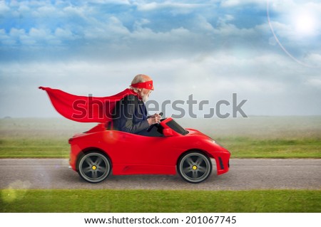 senior superhero with mask and cape driving a toy sports car