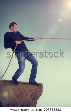 man pulling rope tug of war on a cliff edge adversity concept