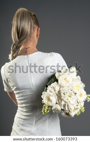 Back view of woman in white dress with a bouquet isolated on gray background