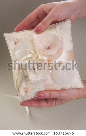 White wedding small satin pillow for rings on woman's hands on gray background