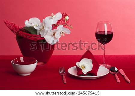 Table setting with white orchid flowers on red tablecloth on red background