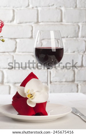 Table setting with white orchid flower on red tablecloth on brick wall background