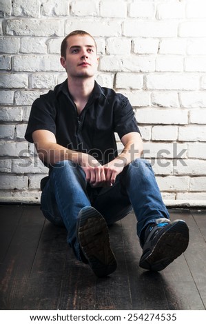 Handsome young man sitting on the floor near the white brick wall