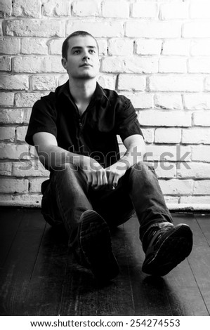 Handsome young man sitting on the floor near the white brick wall, toned black and white