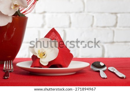 Table setting with white orchid flowers on red tablecloth on brick wall background