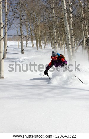Active woman skiing through deep powder snow and aspen trees in the Utah mountains, USA.