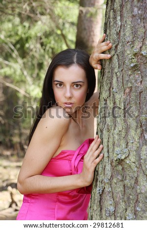 A beautiful woman in fashionable clothes stands near a tree in the forest.