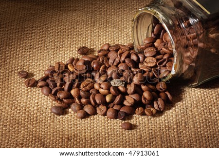 Glass jar. The corns of coffee are spilled on a table.