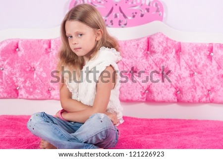 Little girl in jeans sitting on a pink bed