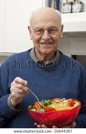 Senior man eating a healthy salad at the kitchen