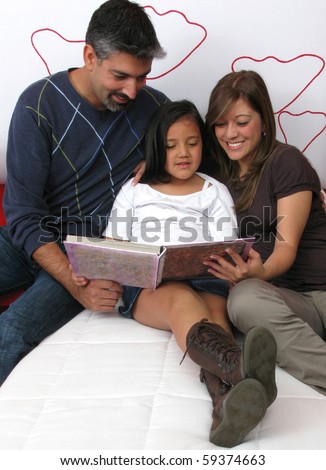 Family reclining in bed reading book together
