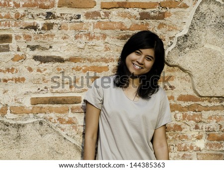 Young pretty girl posing and smiling while standing near brick wall