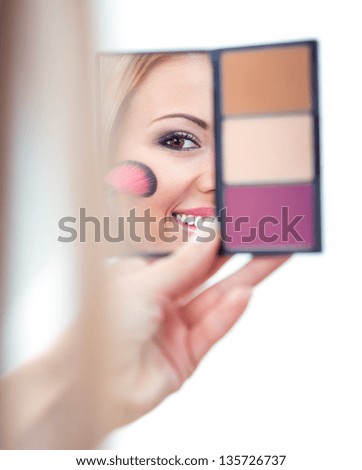 Woman applying cosmetics to her face with the help of cosmetic brush, isolated on white