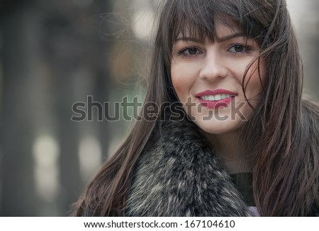 Portrait of a young smile woman wearing fur with a blurred nature background. Close up, head shot of cute girl, outdoors