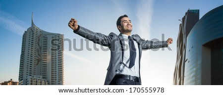 Successful businessman with his arms wide open. Joyous man  with success perspective, modern buildings at background