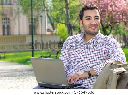Happy man sitting on bench and using laptop in a park. Profile - sideways of a guy