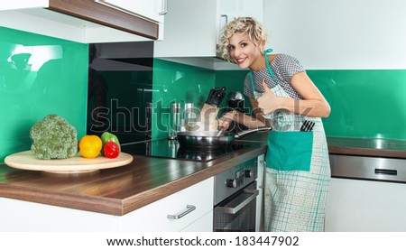 Young woman cook or housewife gesturing thumbs up in the kitchen at home, prepare healthy food. Happy female with sign OK