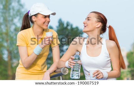Two smiling girl friends in sports clothing drinking water, together doing healthy lifestyle. Outdoors - outside