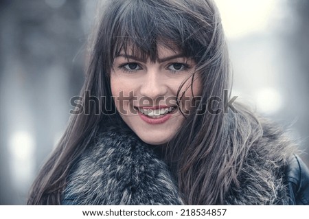 Woman with hair blowing in the wind with a blurred nature background. Winter cold weather, close up shot of beautiful girl, outdoors