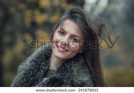 Portrait of a young smile woman wearing fur with a blurred nature background. Close up, head shot of cute girl, outdoors
