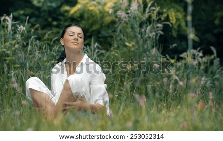 Young relaxing woman sitting in the grass with closed eyes, outdoors, daylight. Beautiful girl relaxing