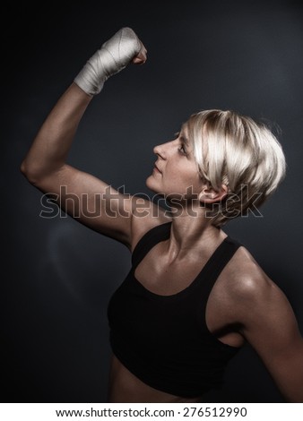 Sporty woman showing her biceps on dark gray background