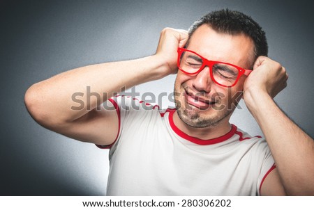 Funny disappointed young man crying over gray dark background