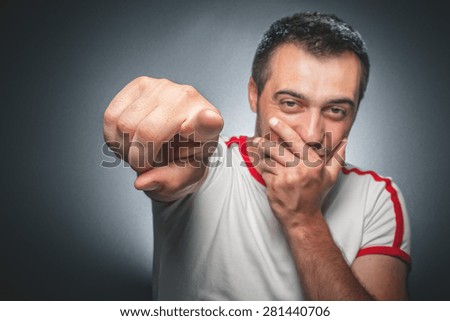Young man pointing and laughing at you. Funny crazy guy over gray dark background