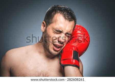 Boxer feel hurt and pain crying, knockout situation. Dark gray background. Beaten fighter with red sport boxing gloves. Waist up of defeated kickboxer