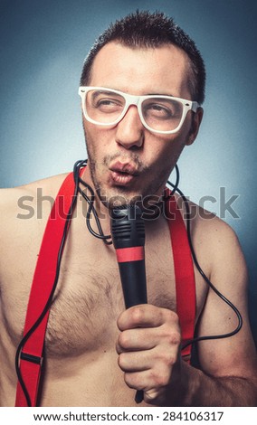 Funny party man, guy holding microphone. and singing. Young trendy man with disco eyewear  over dark blue gray background, studio shot