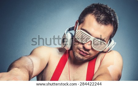 Dj playing the music, guy is ready for party. Young trendy man listening music with headphones over dark blue gray background, studio shot
