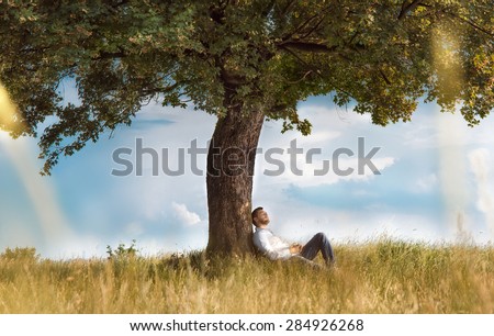 Human sitting under tree. Man repose on grass in nature. Outdoors - outside. No stress, carefree