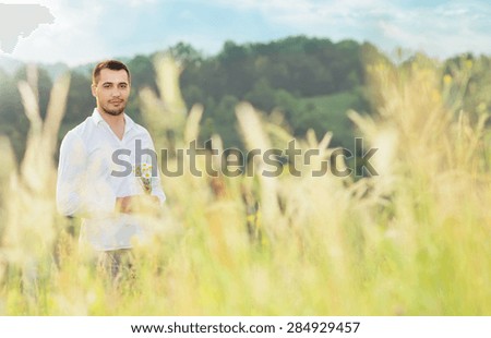 Beautiful young man standing in a grass in white shirt holding flowers, outdoors. Male beauty natural concept with copyspace for text. Seducer