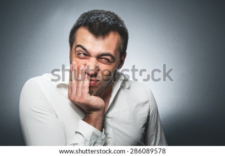 Confused young man over dark gray background. Studio shot. Guy make a funny face