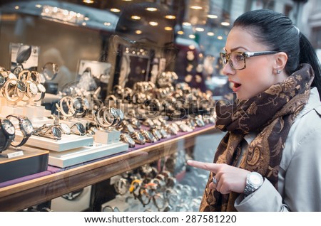 Excited young woman looking to showcase or shop window. Shopping girl chooses jewelry in store